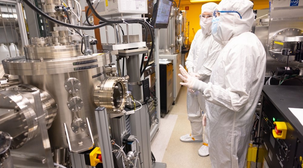 Scientists in full-body white coveralls inspect equipment in a cleanroom