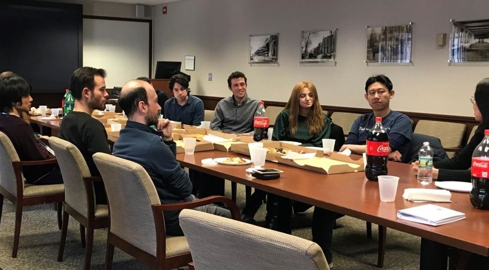 People sit at a long table in a conference room with food