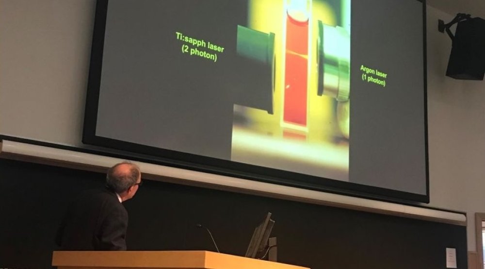 A man at a podium looks at a PowerPoint slide