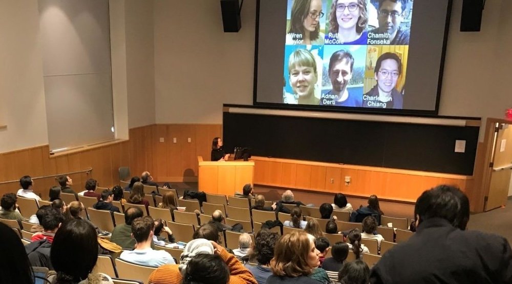 People in an auditorium look at a PowerPoint slide