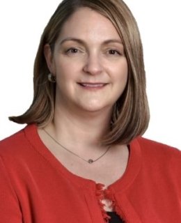 Headshot of a fair-skinned person with straight shoulder-length brown hair and a red top. They are wearing a small pendant on a chain.