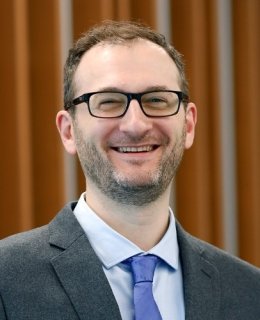 Smiling light-skinned man in dark-rimmed glasses wearing a suit and tie