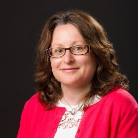 Smiling person with brown hair and glasses