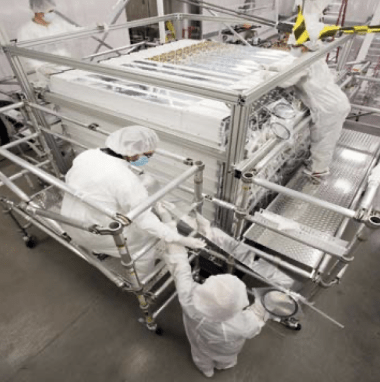 Scientists in protective garb stand by equipment