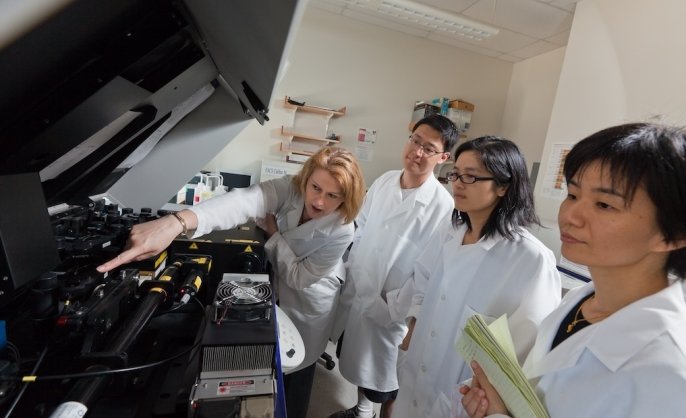 A scientist points to an instrument while three others look on