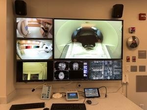 A monitor displays multiple views of different rooms and brain readouts