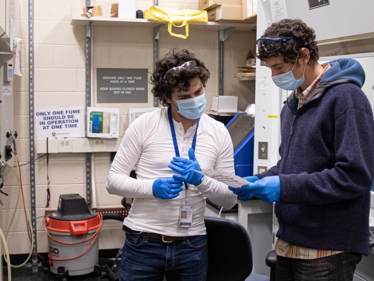 Two masked people in a lab examine a paper