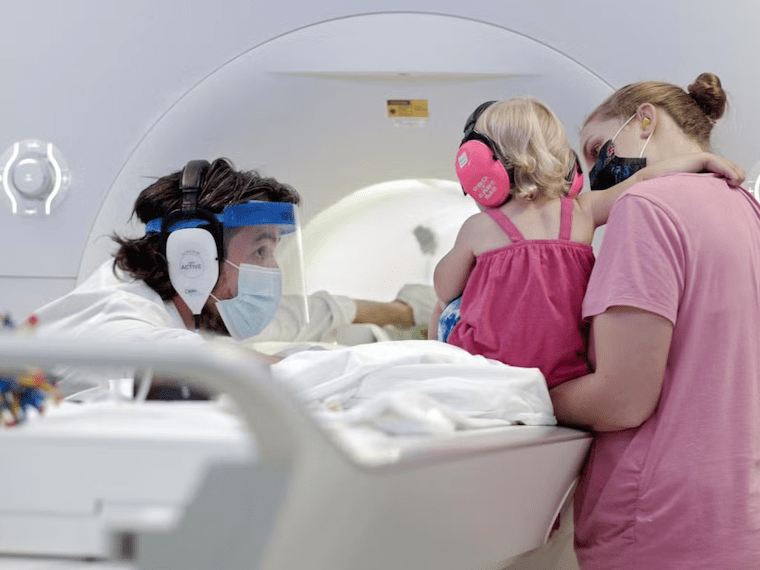 A toddler, parent, and researcher in front of an MRI machine